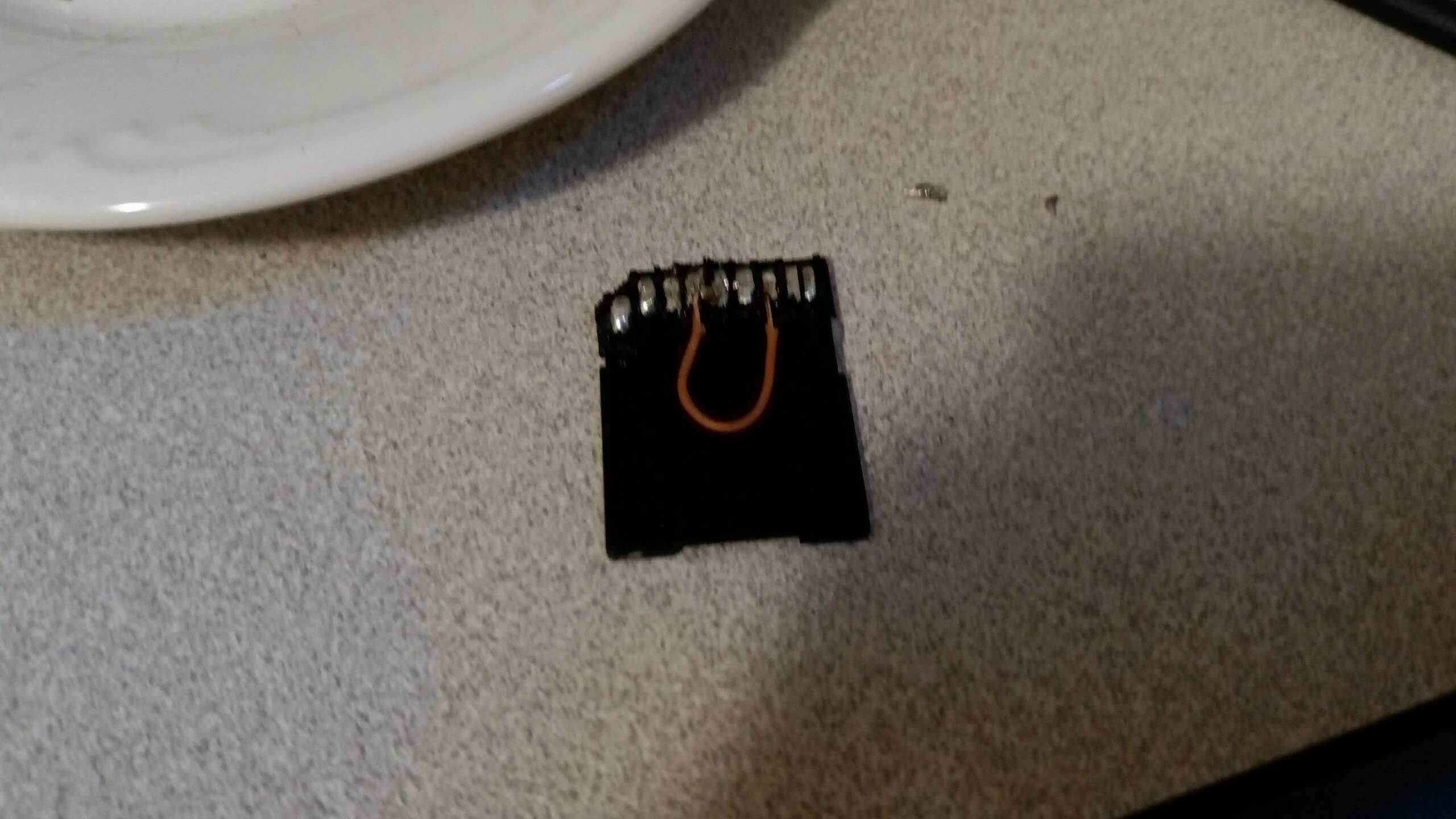 Prepped SD card. It's face-down on the table with a wire between two of the contacts.