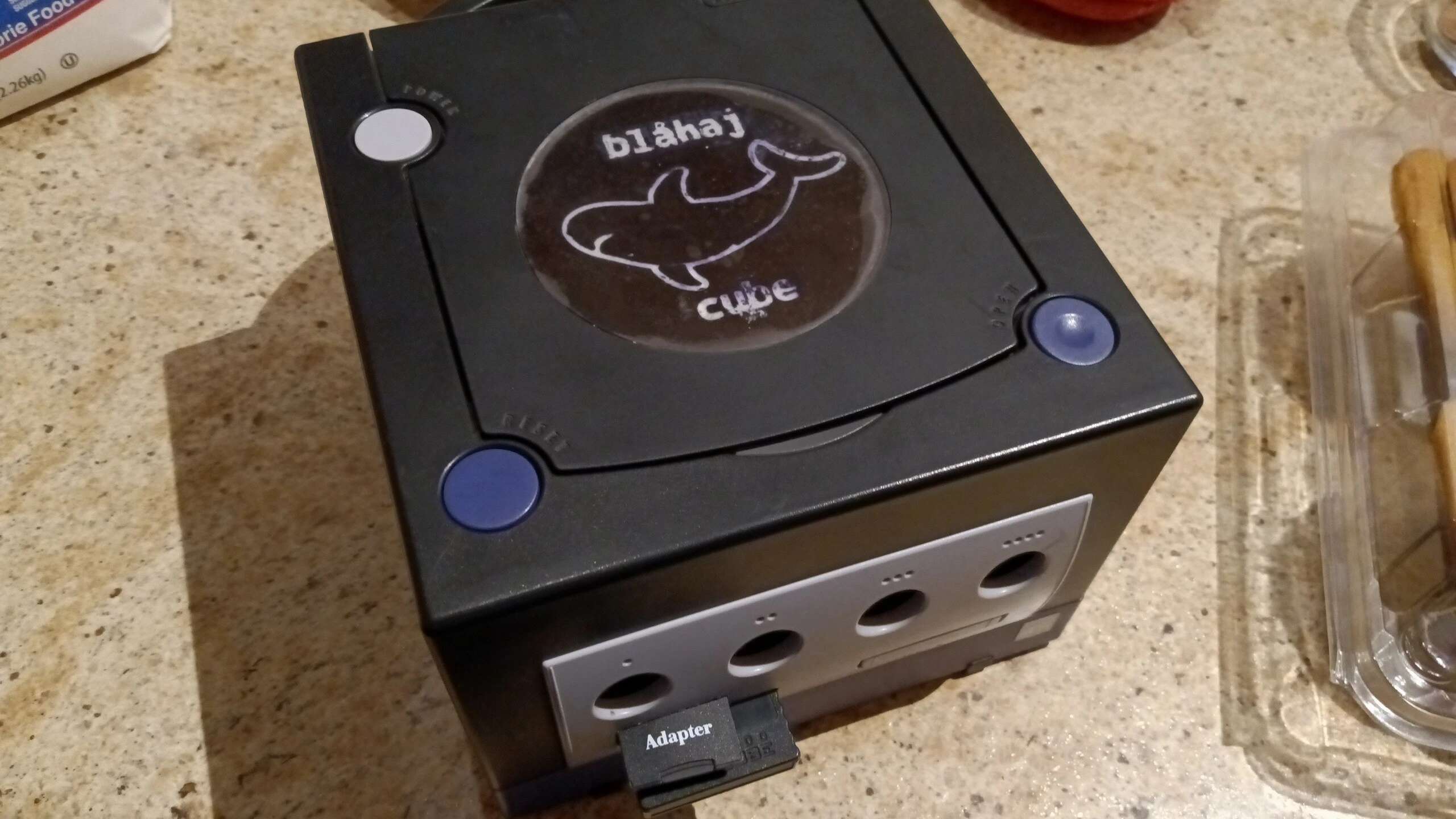 GameCube with purple top buttons but a black body. The GameCube jewel is replaced with a blahaj one.