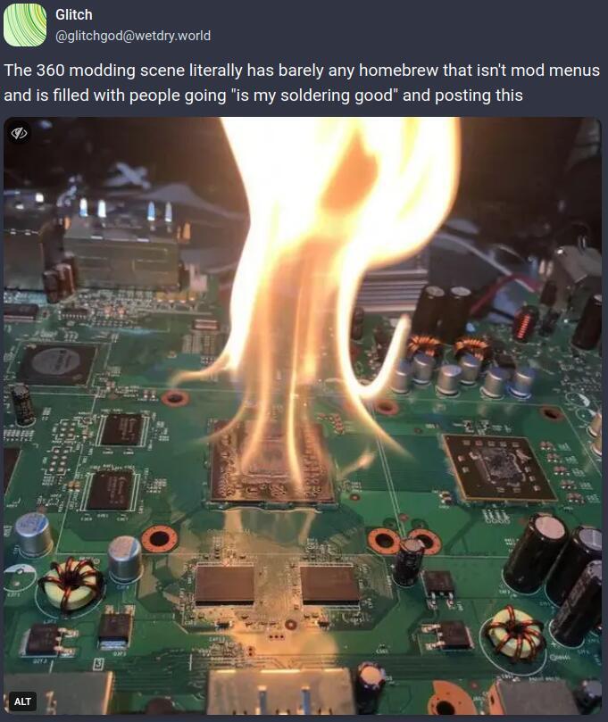 Mastodon post from user @glitchgod@wetdry.world. The post reads "The 360 modding scene literally has barely any homebrew that isn't mod menus and is filled with people going "is my soldering job good" and posting this". A photo is attached. In it is an Xbox 360 with a GPU chip that has been set aflame. The board appears to be one of the fat models.