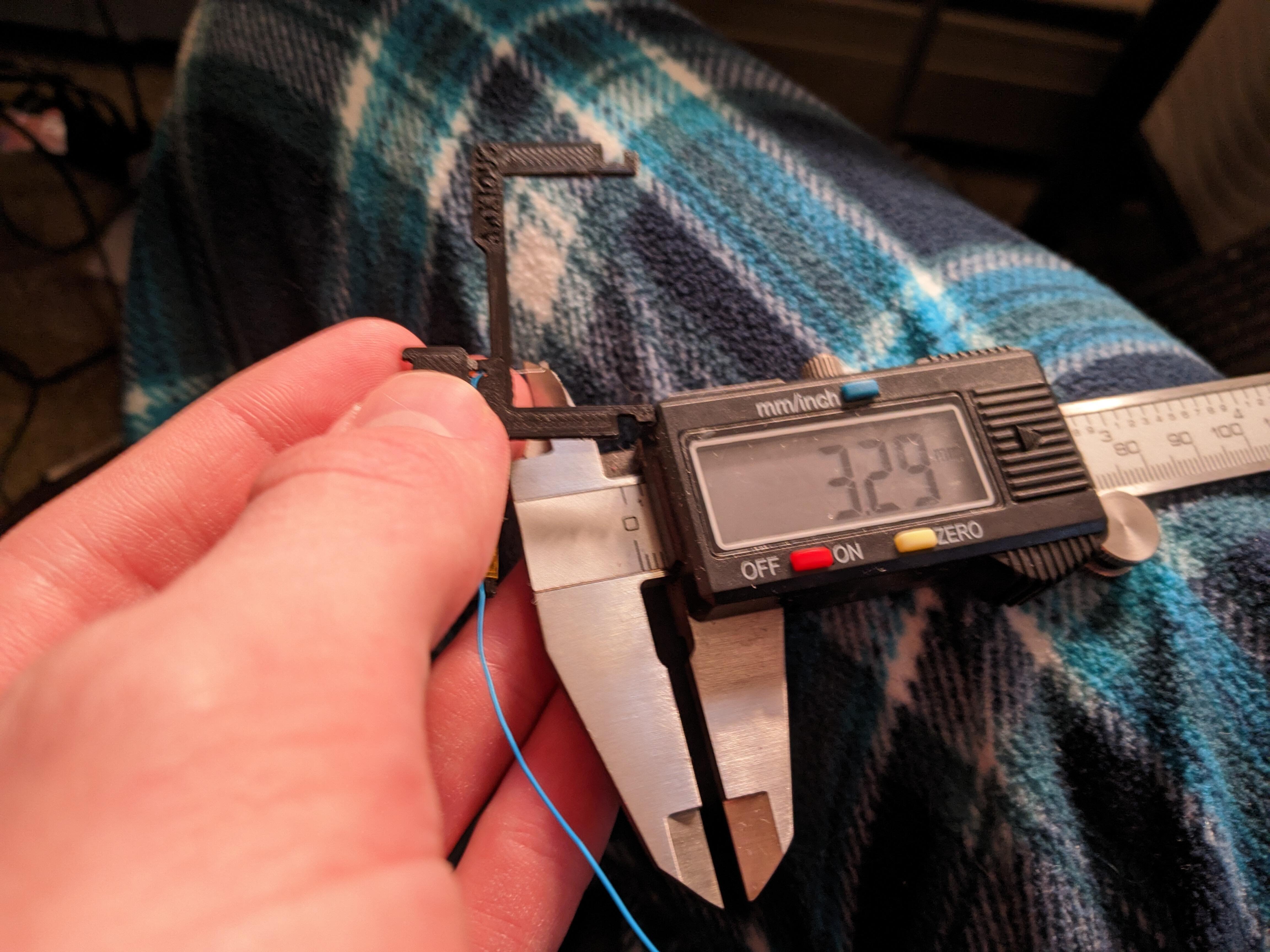 Me in my blue flannel pajamas measuring the small bit of wire that will poke under the APU. I'm using digital calipers and they're reading 3.29mm. This isn't very accurate as I don't have a good grip in the photo. The wire has already been threaded through its designated hole in the left half of the postfix adapter. The quality of the printed part isn't the greatest, but it's servicable.