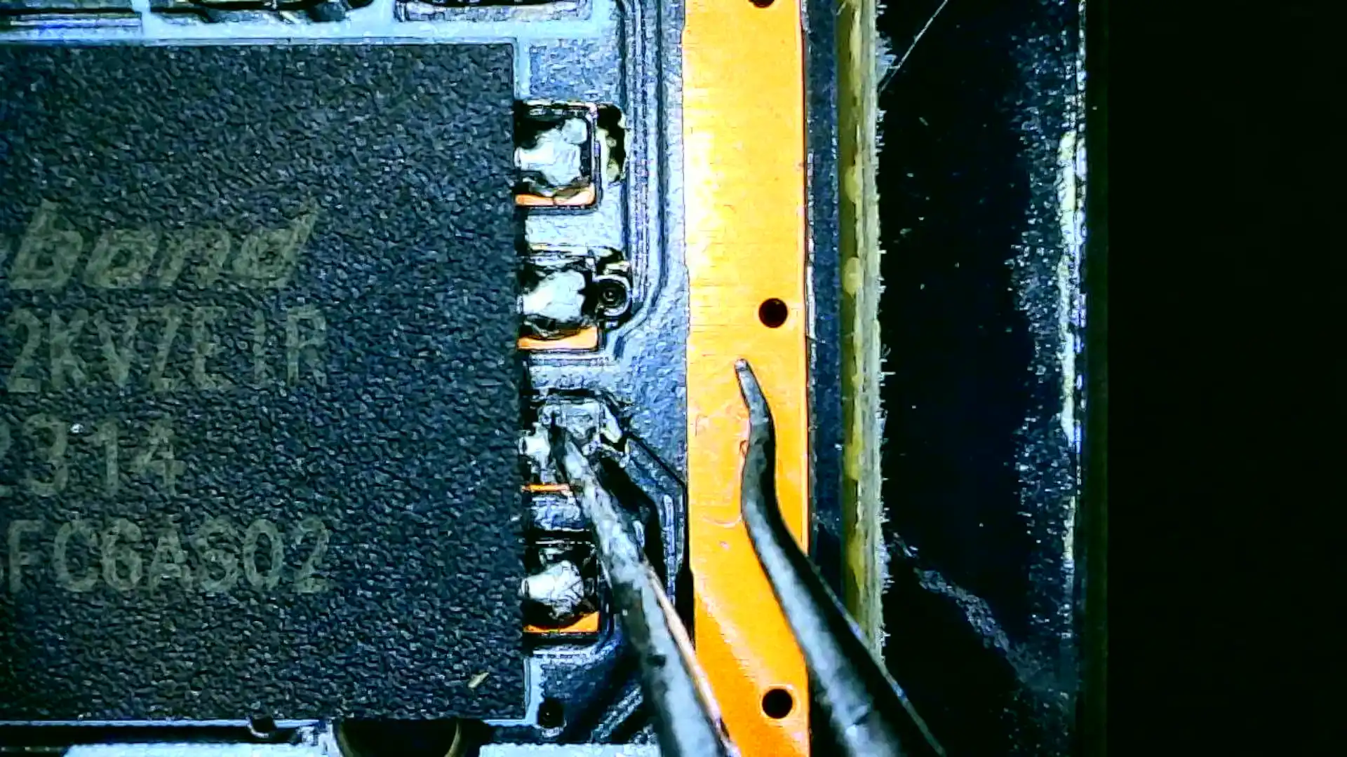 A pair of tweezers bridges the second pin from the bottom out of four on the right side of the Winbond SPI to the ground trace that runs around the mainboard.